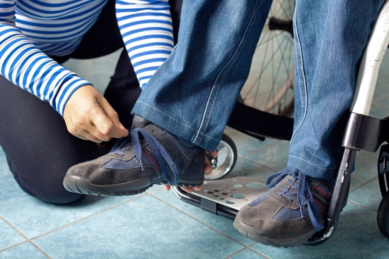Support worker tying shoe laces of NDIS participant in wheelchair