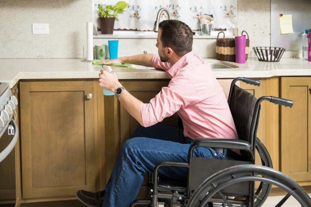 Disabled man in wheelchair wiping down kitchen benches at home