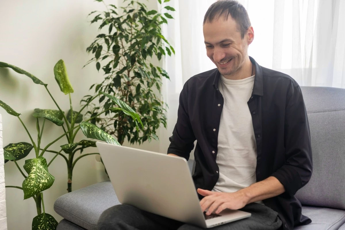 Happy man using laptop at home while sitting on couch
