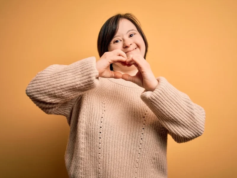 Happy woman with down syndrome making love heart shape with hands
